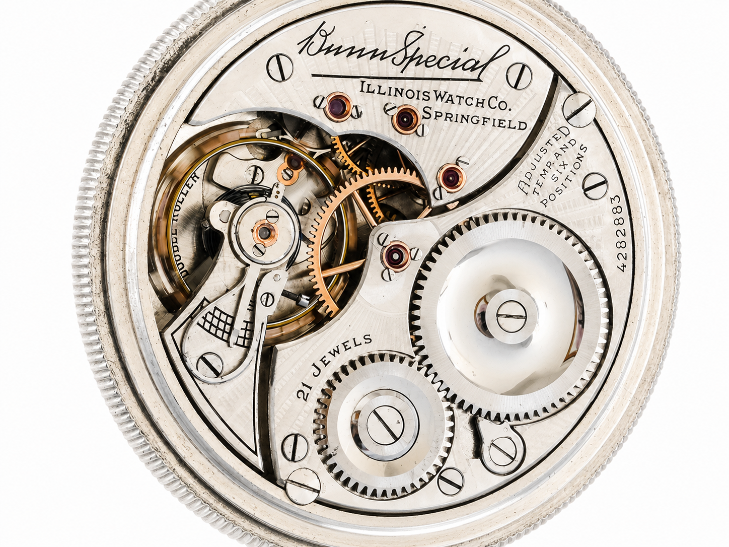 Open pocket watch movement showing brass gears, jeweled components, and engraved steel plate with maker details and "21 Jewels" marking.