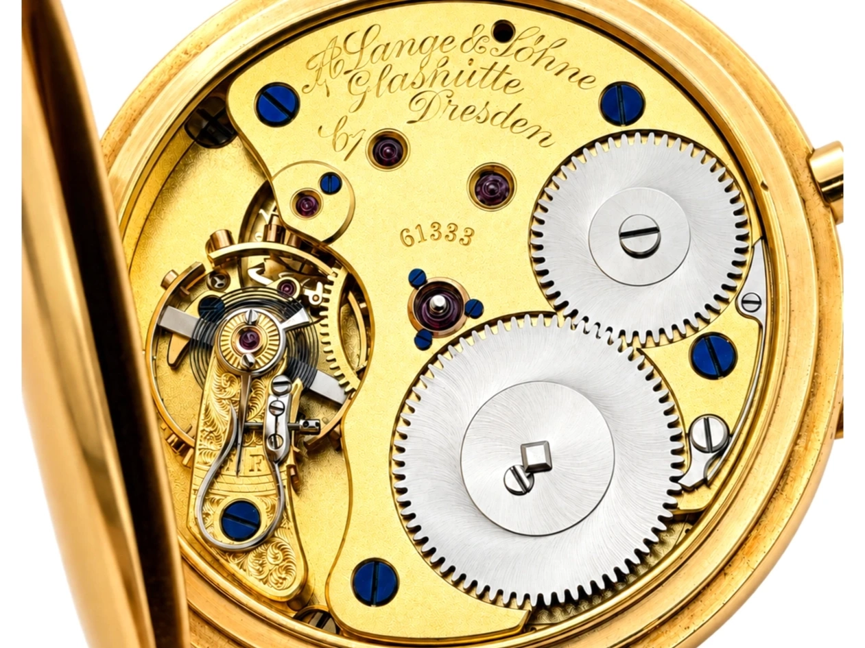 Interior mechanism of pocket watch showing gilt brass movement with jewels, escape wheel, and gears.