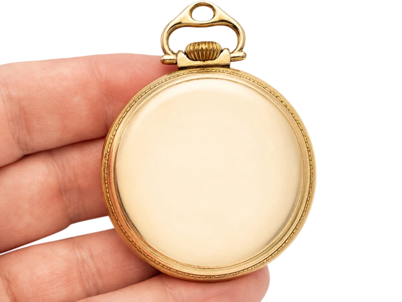 Gold pocket watch case with bail held in hand, showing blank cream-colored dial.