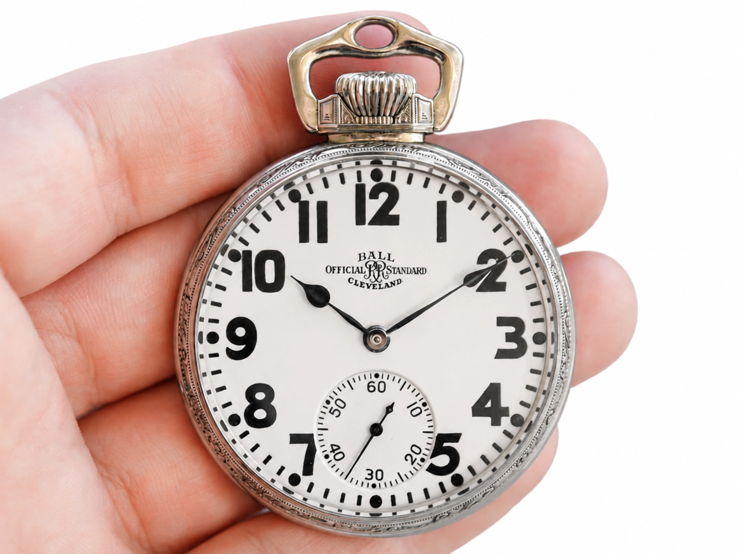 Open-face pocket watch with white dial, bold Arabic numerals, subsidiary seconds dial, and metal case held in hand.