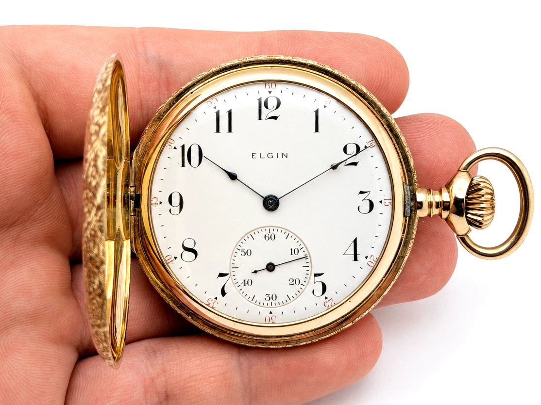 Gold open-face pocket watch with white dial, Arabic numerals, subsidiary seconds dial, held in hand.