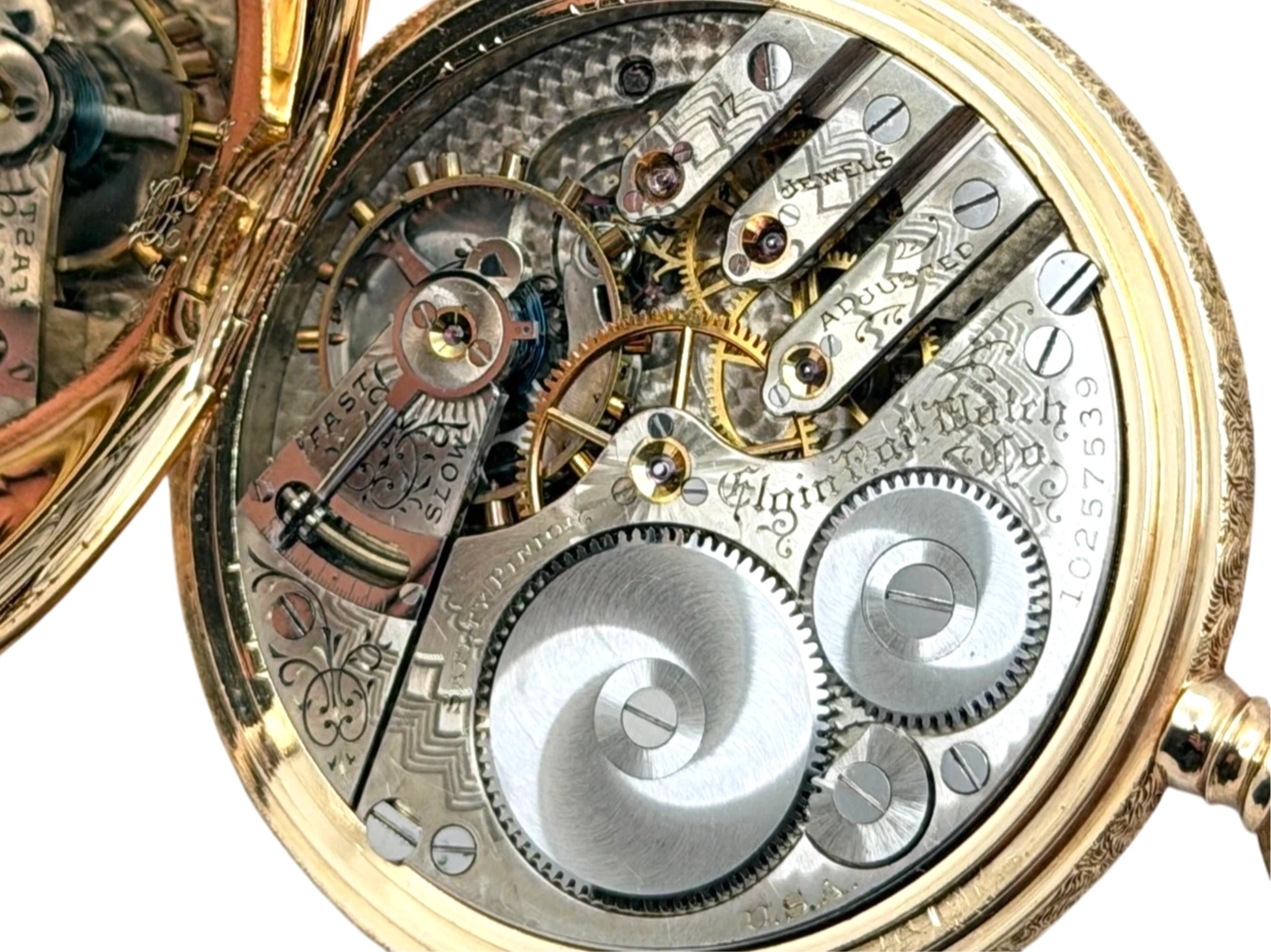 Open pocket watch movement showing large polished balance wheel, multiple jewels, and ornate engraved plates.
