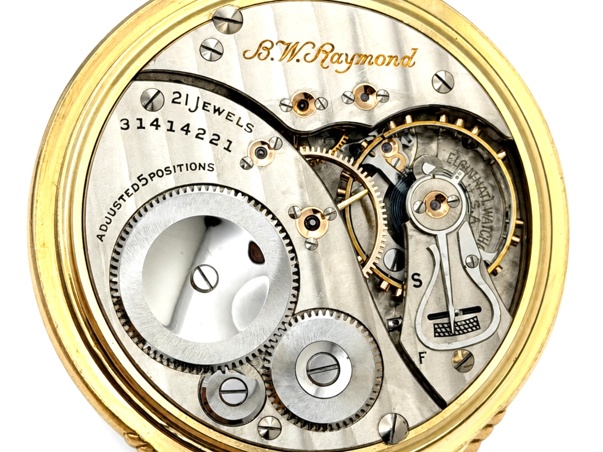 Exposed pocket watch movement showing 21 jewels, gears, and balance wheel in gold-filled case.
