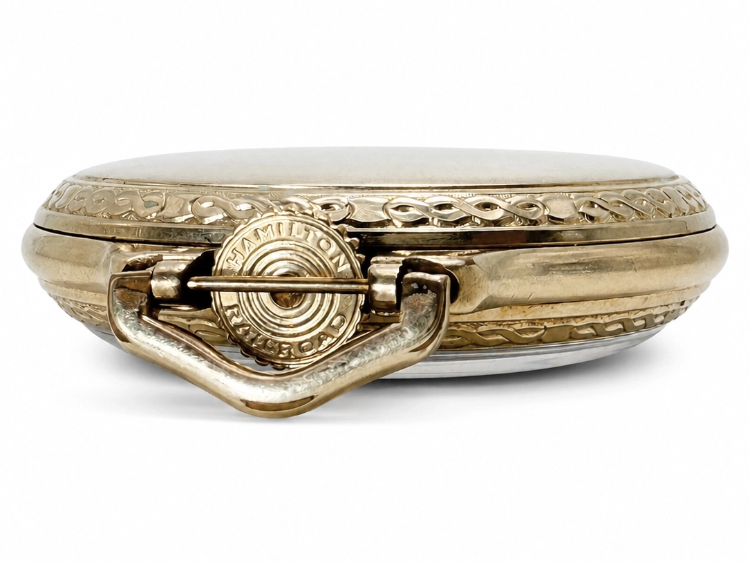 Gold pocket watch case closed showing ornate decorative clasp and relief patterning on the edge.