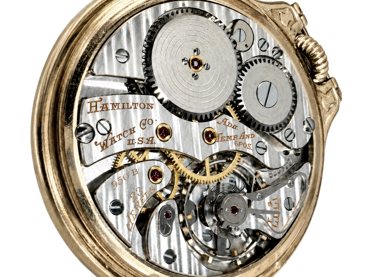 Open pocket watch movement showing gears, balance wheel, and ruby jewels on Hamilton watch co case.