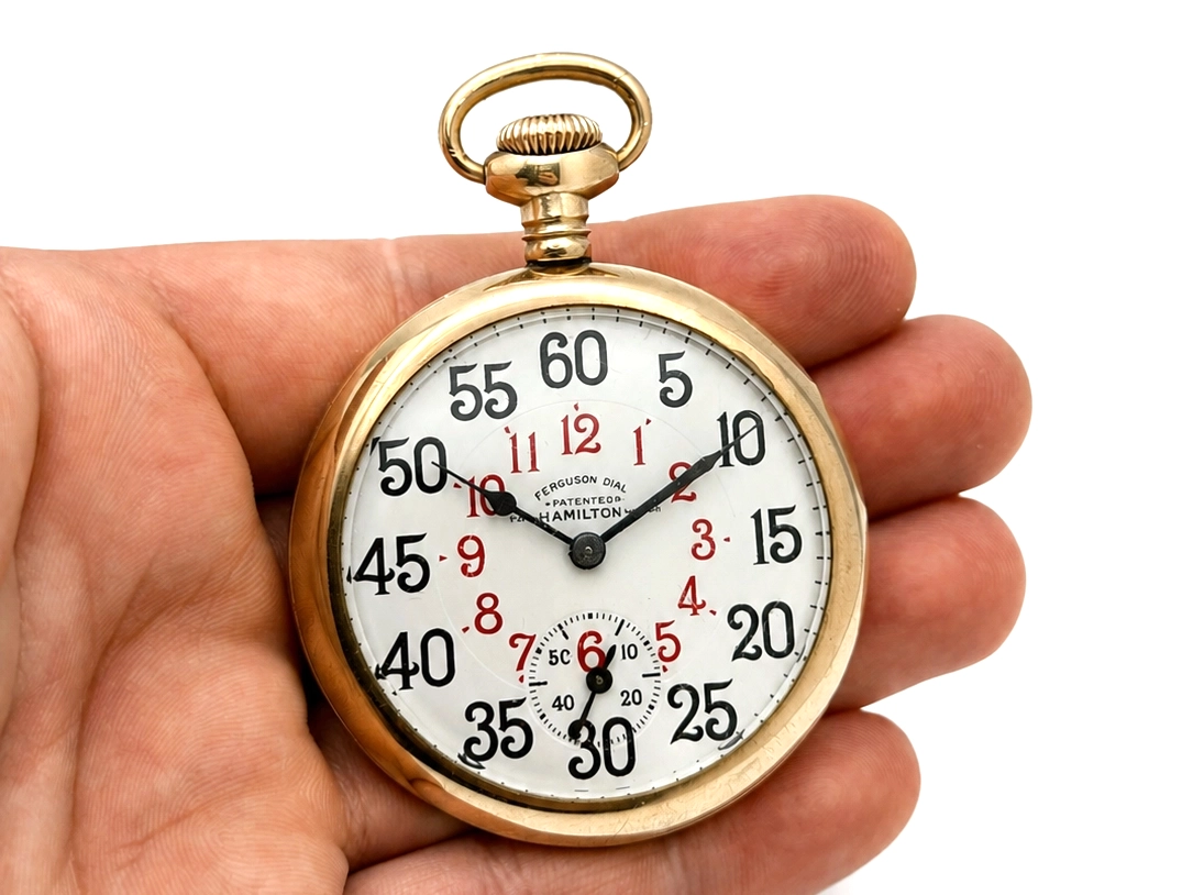 Gold-tone pocket watch with white dial showing black Arabic numerals, red accents, and subsidiary seconds dial.