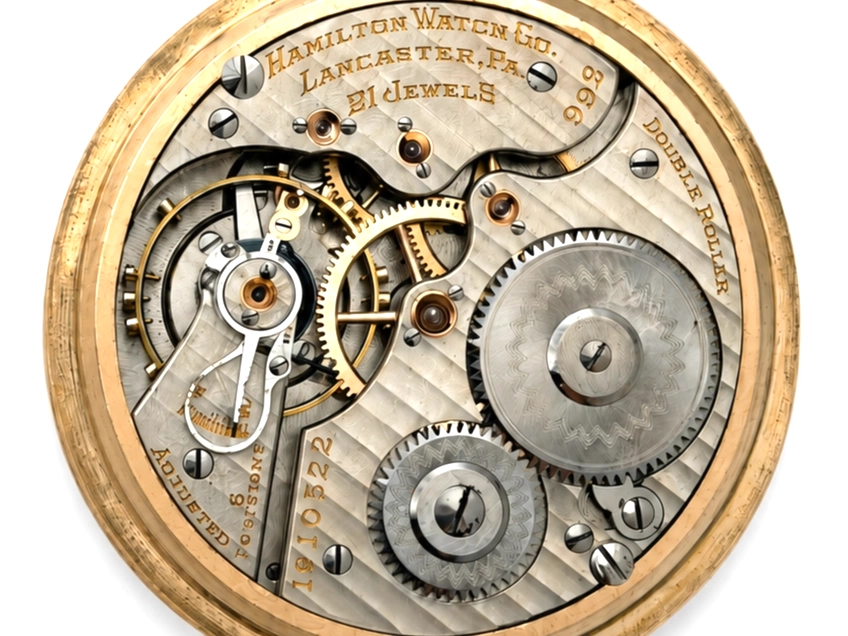 Open pocket watch movement showing exposed gears, jewels, and balance wheel in brass case.