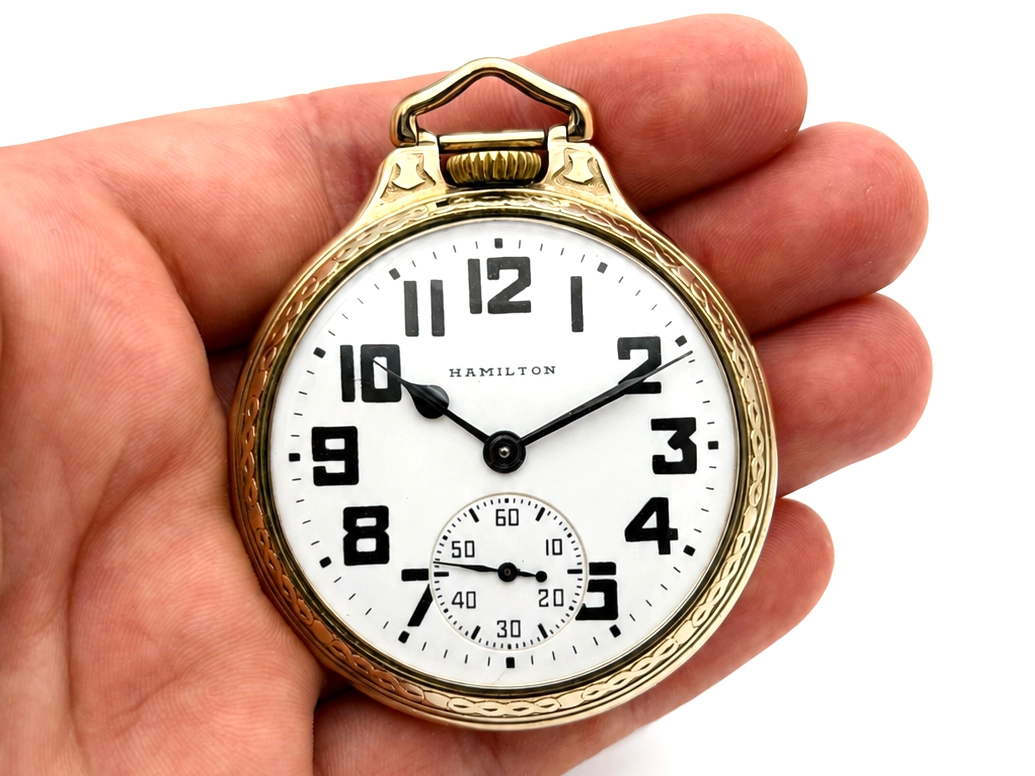 Gold-tone pocket watch with white dial, black Arabic numerals, and subsidiary seconds dial at 6 o'clock.