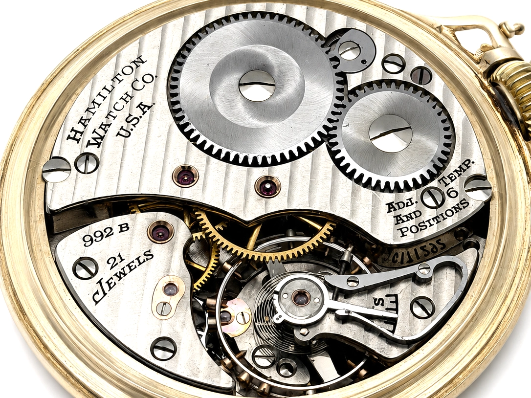 Hamilton pocket watch movement with exposed gears, jewels, and escapement visible through open case back.