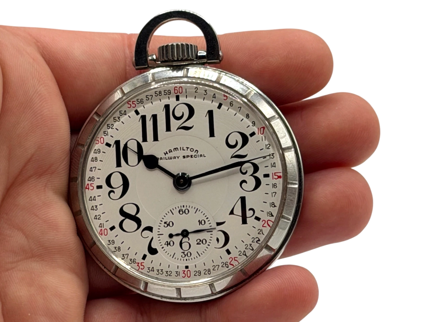 Open pocket watch with Arabic numerals, subsidiary dial, and lugs held in hand against black background.