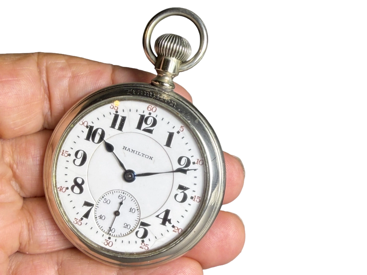 Open-face pocket watch with white dial, Arabic numerals, and subsidiary seconds subdial, held in hand.
