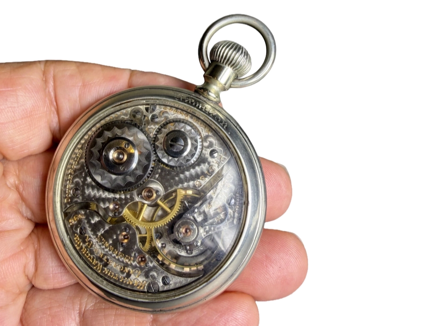 Open pocket watch movement showing exposed gears, jewels, and balance wheel with metal case back removed.