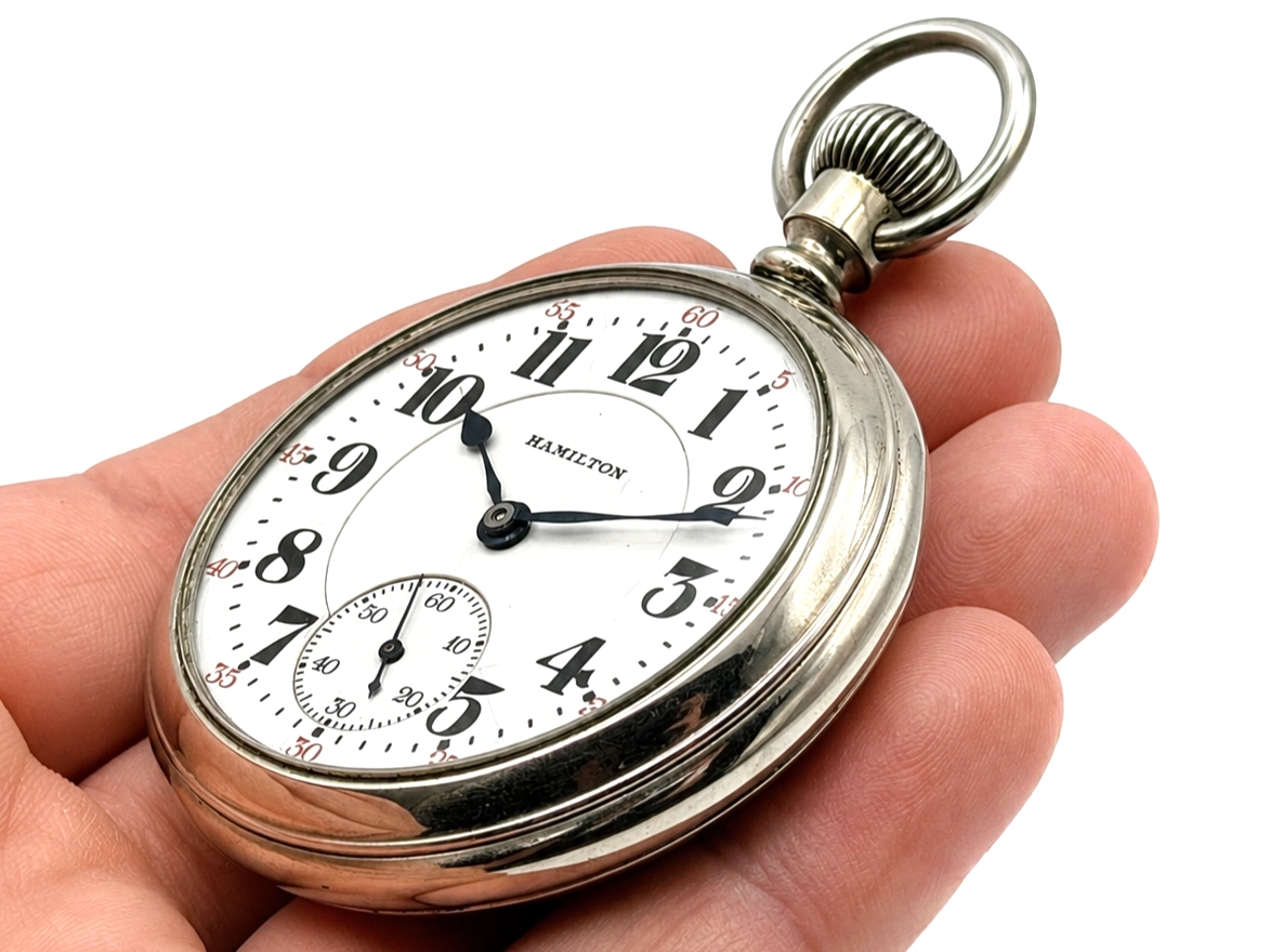 Open face pocket watch with white dial, Arabic numerals, subsidiary seconds dial, and metal case in hand.
