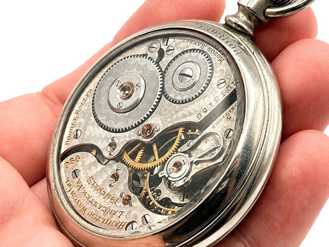 Open pocket watch movement showing jeweled gears, polished steel plates, and gold balance wheel.