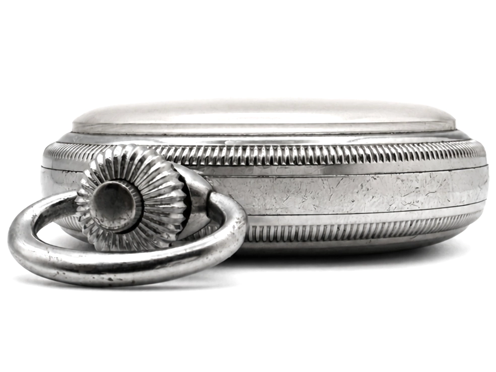 Closed metal case with engine-turned bands and decorative shell-form ring, shown open to reveal oval box shape.