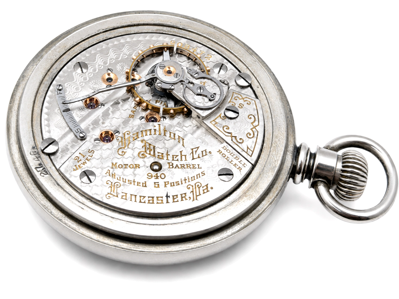 Open pocket watch movement showing motor barrel, jewels, and engraved metal plate with text.