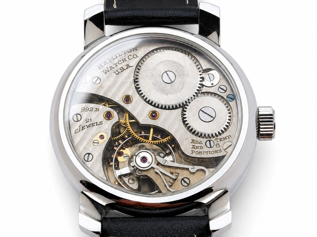 Open caseback revealing mechanical movement with exposed gears, jewels, and balance wheel on black leather strap.