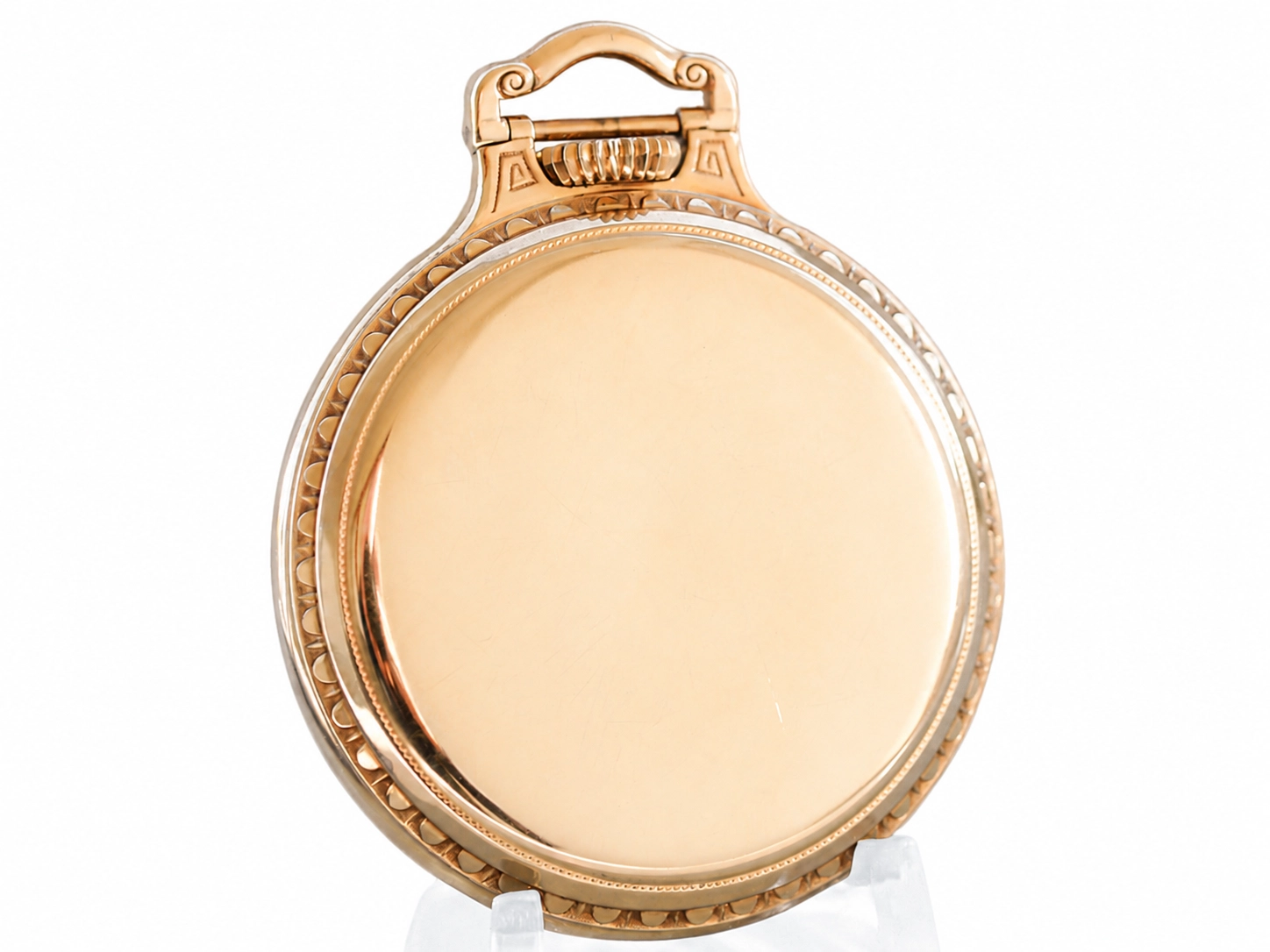 Polished gold pocket watch case back with ornate scrollwork and decorative beading around the edge.