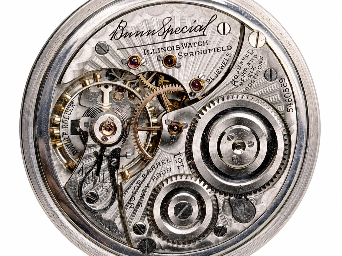 Open pocket watch movement showing brass gears, jeweled bearings, and engraved mainplate with visible hairspring.