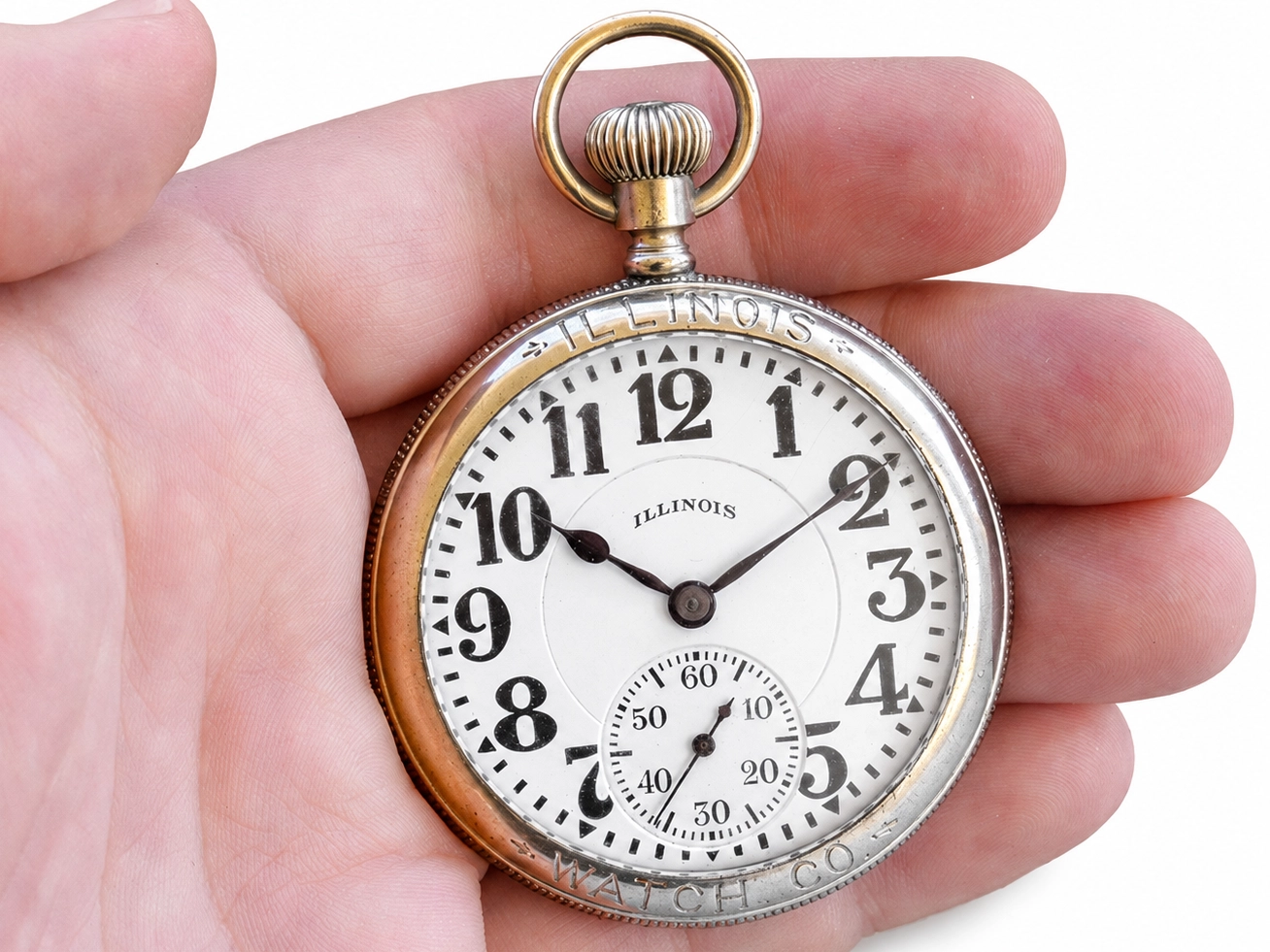 Open-face pocket watch with white enamel dial, Arabic numerals, and subsidiary seconds dial, held in hand.
