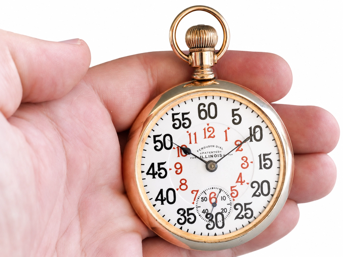 Gold-tone stopwatch with white dial, black and red numerals, subsidiary seconds dial, held in hand.