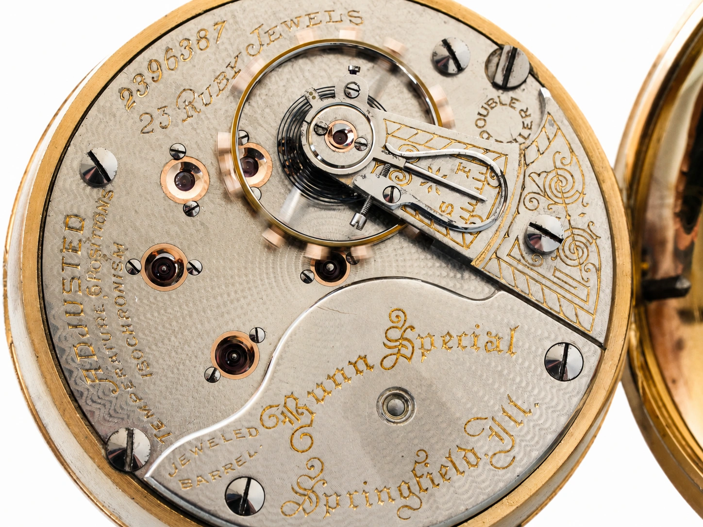 Open pocket watch movement showing jeweled balance, barrel spring, and gold lettering on silvered plate.