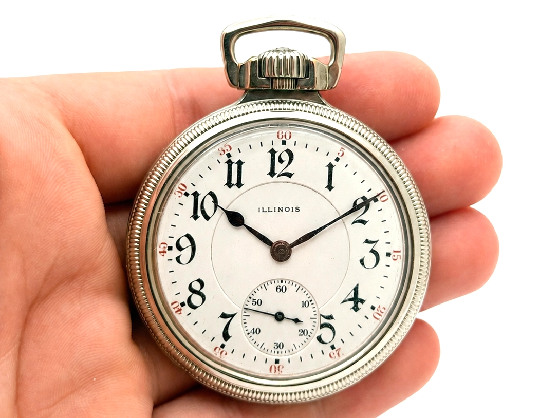 Silver pocket watch with cream dial, Arabic numerals, subsidiary seconds dial, and ornate bow in hand.