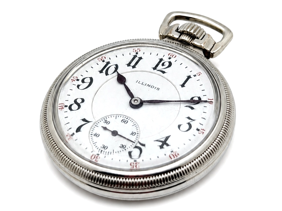 Open-face pocket watch with white dial, Arabic numerals, subsidiary seconds dial, and metal case visible.
