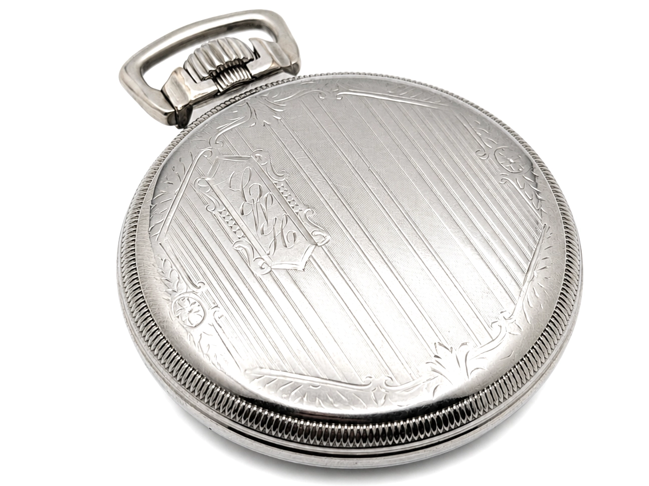 Closed silver pocket watch case back with ornamental engraved design and vertical striping pattern.