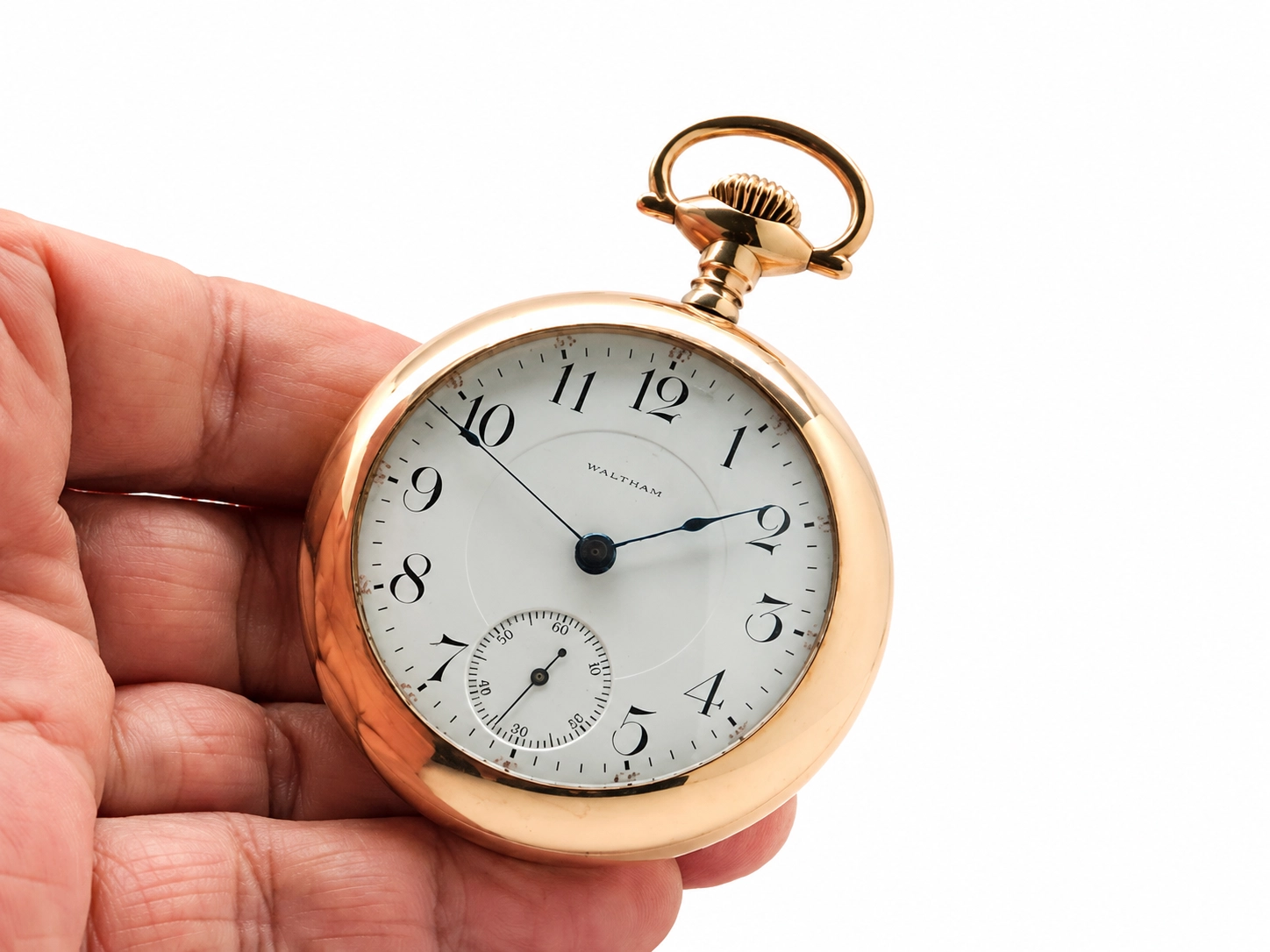 Open-face pocket watch with white dial, Arabic numerals, subsidiary seconds dial, and polished rose gold case held in hand.