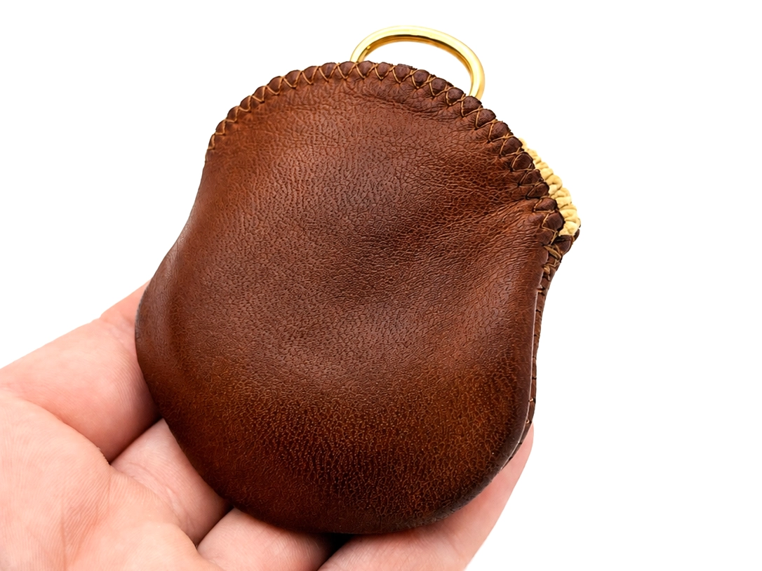 Brown leather watch pouch with brass ring held in hand.