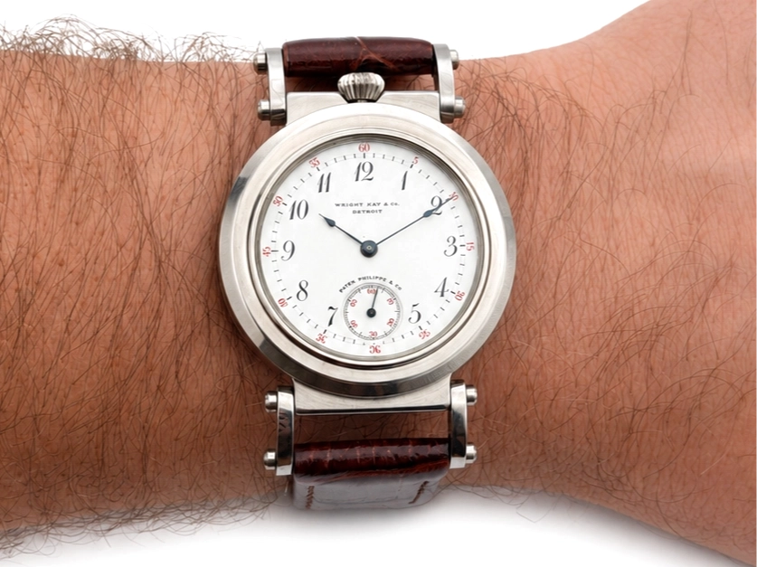 Wristwatch with white dial, Arabic numerals, small seconds subdial, and dark leather strap on wrist.