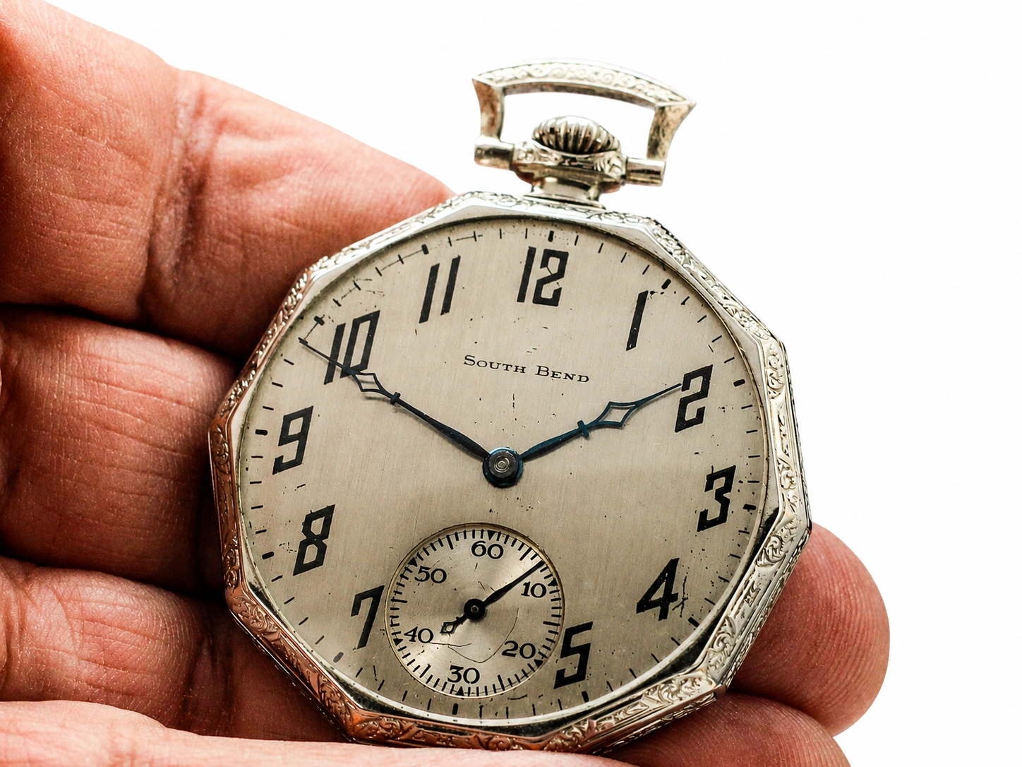 Silver octagonal pocket watch with Arabic numerals, subsidiary seconds dial, and ornate case held in hand.