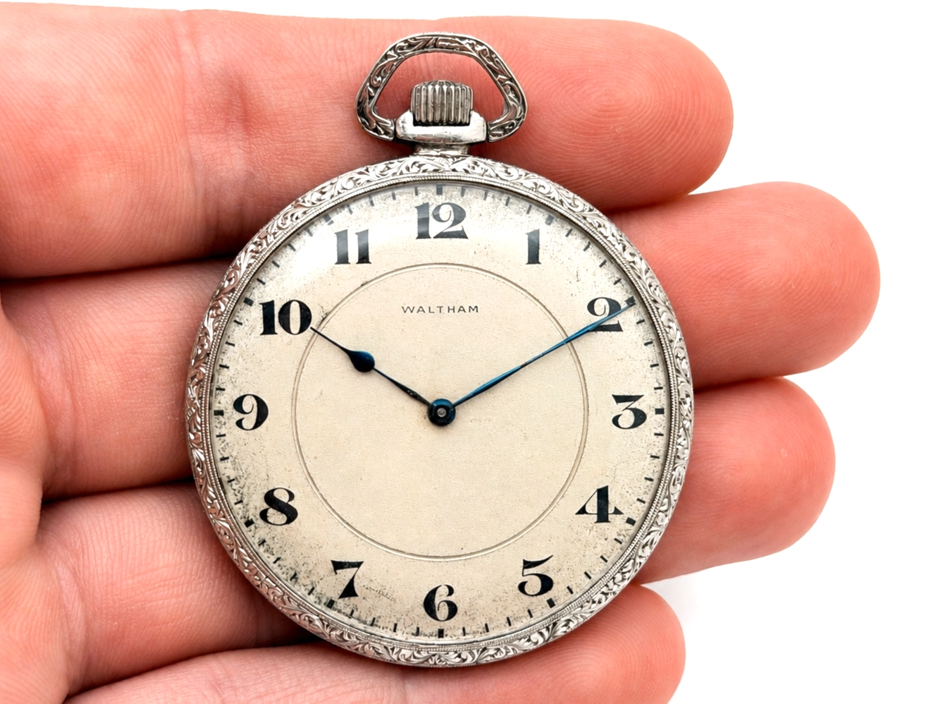 Waltham pocket watch dial with Arabic numerals and ornate silver case held in hand.