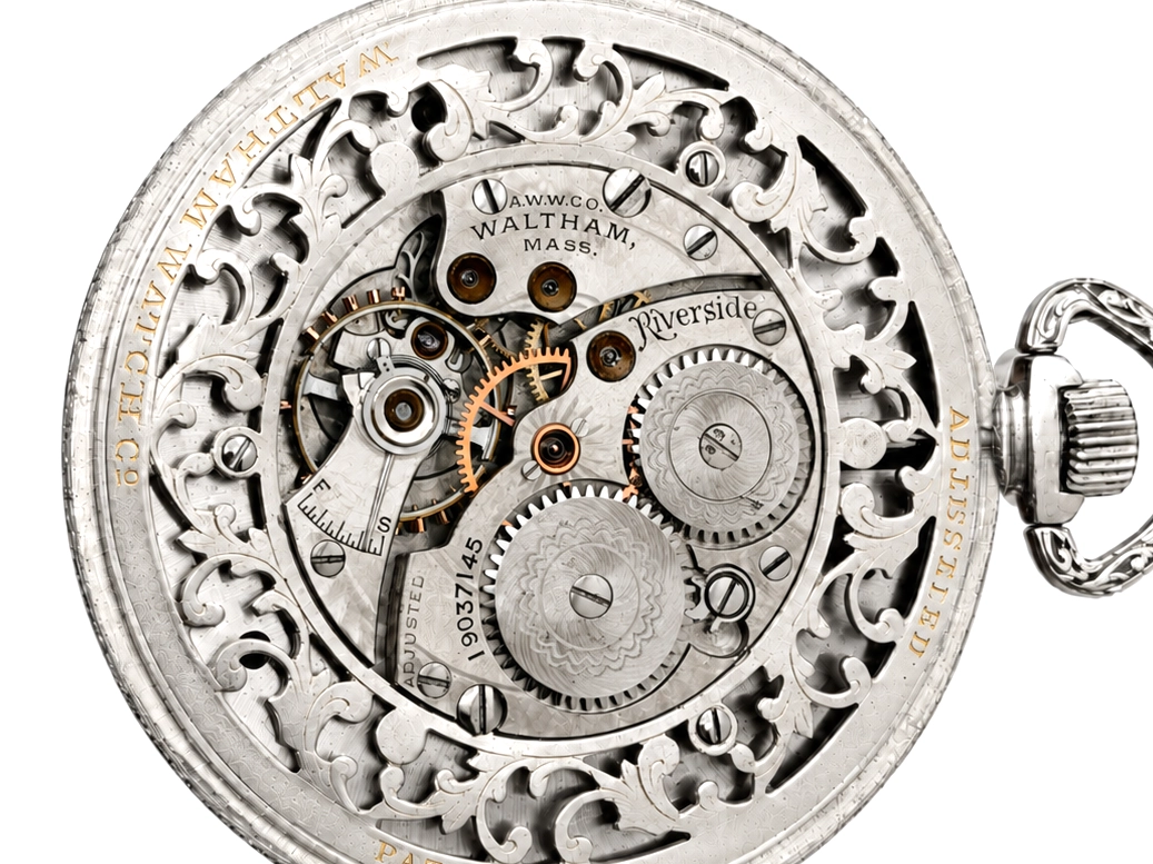 Open pocket watch movement showing ornate plate, gold gears, and Waltham, Mass. inscription with Riverside model marking.