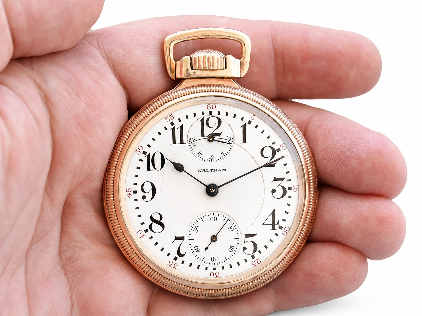 Rose gold pocket watch with white dial, black Arabic numerals, subsidiary seconds dial, and Waltham inscription.