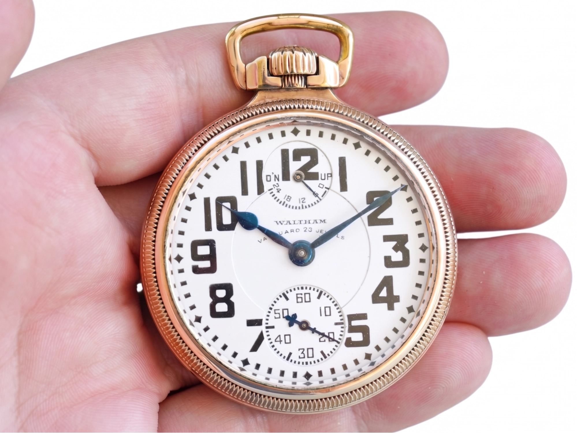Waltham pocket watch with white dial, bold Arabic numerals, subsidiary seconds dial, and blue hands held in palm.