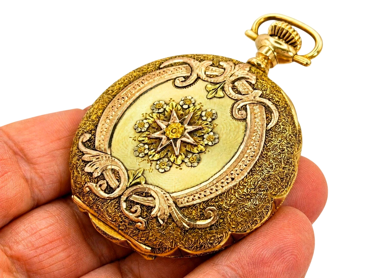 Gold pocket watch case with ornate floral and scrollwork engraving, held in hand.