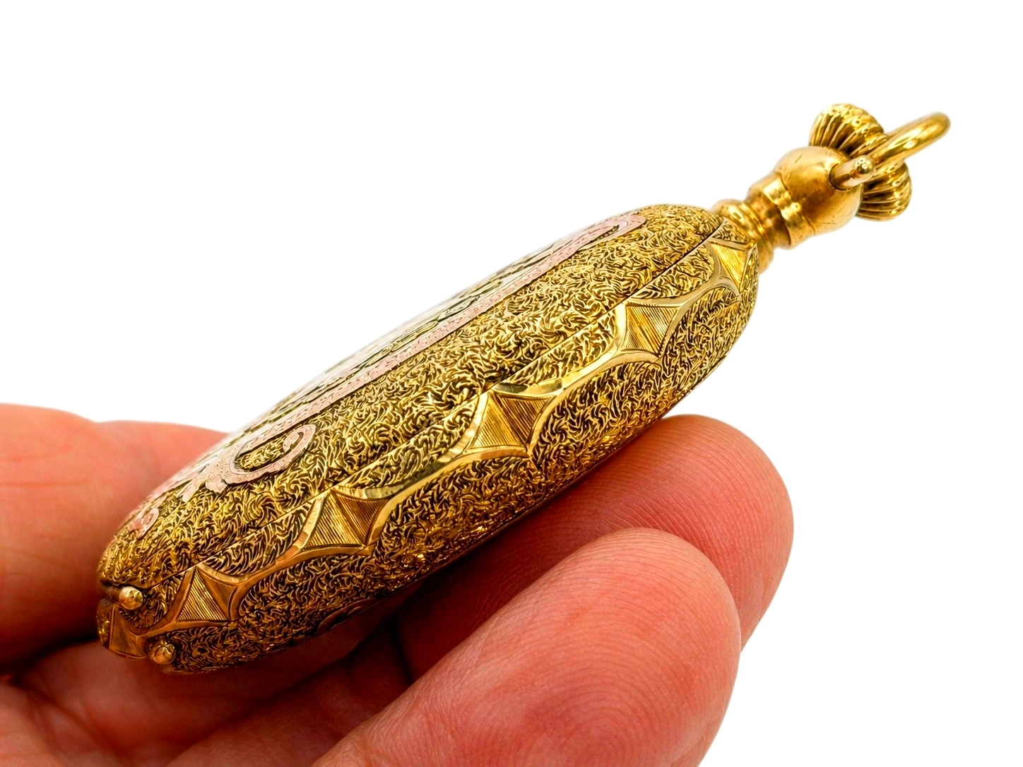 Gold pocket watch case with ornate engraved scrollwork and geometric diamond motifs, shown in hand with decorative ball bail.