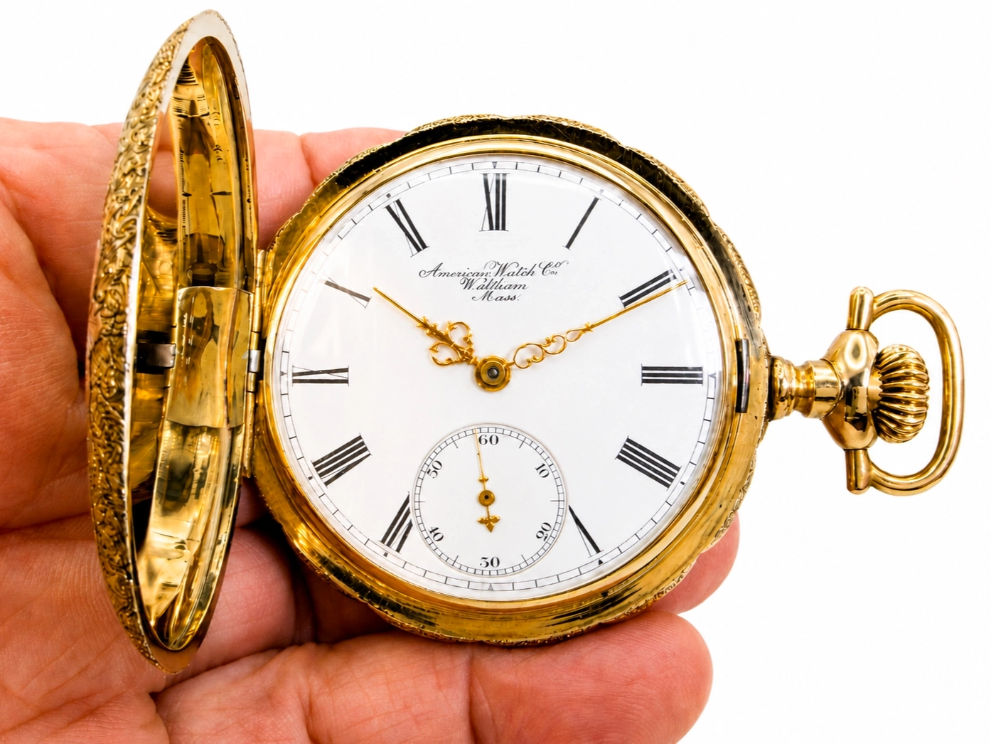 Open gold pocket watch with white dial, black Roman numerals, subsidiary seconds dial, and decorative ornate cover held on left side.