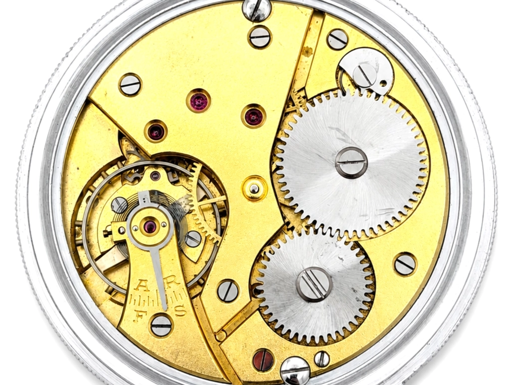 Open pocket watch movement showing yellow gilt plate with exposed balance wheel, steel gears, and ruby jewels.